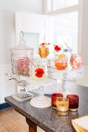 Beautifully arranged wedding cocktail display with drinks in ornate glasses, set on vintage-style white stands.