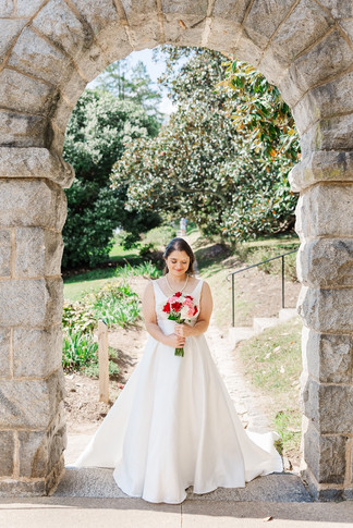 Bride standing under a stone archway, holding a bouquet at a historic wedding venue in Richmond, VA at Maymont Park