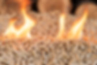A pile of wood pellets on fire. Behind in defocus there is a wall of wood..jpg