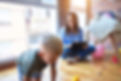 A woman monitors a child playing with toys while smiling.