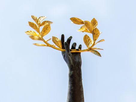 Die Hand einer Statue hält einen vergoldeten Loorbeerzweig in den blauen Himmel. 