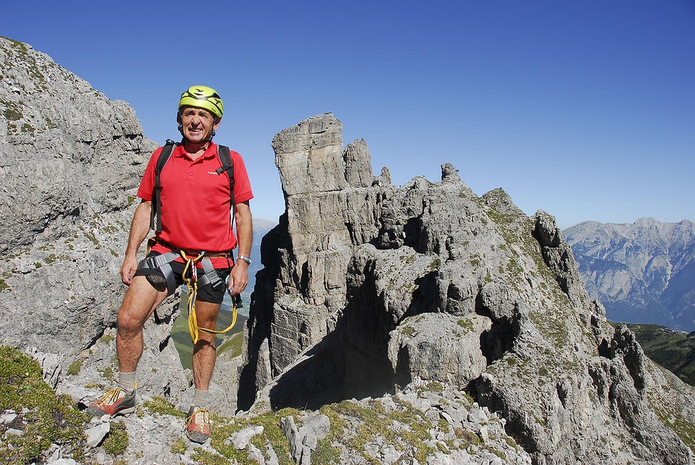 Ein Mann im Rentenalter steht in Bergsteiger-Ausrüstung auf einem Gipfel.