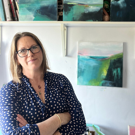 Sarah Granville standing with her arms crossed and smiling at the camera, with a selection of her paintings in the background, Sarah is the person who's website this is.