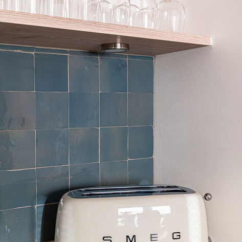 Crème Smeg toaster on a counter with blue tiles and glass. Ateliers de Marine