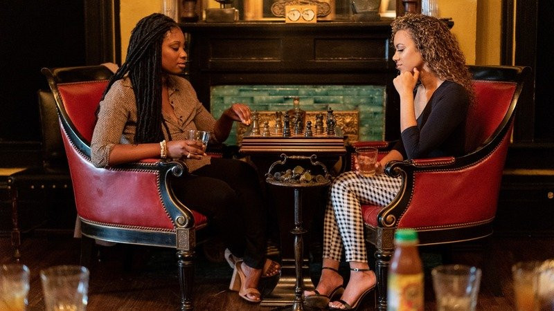Two women play chess in a classy room while enjoying Guidance Whiskey