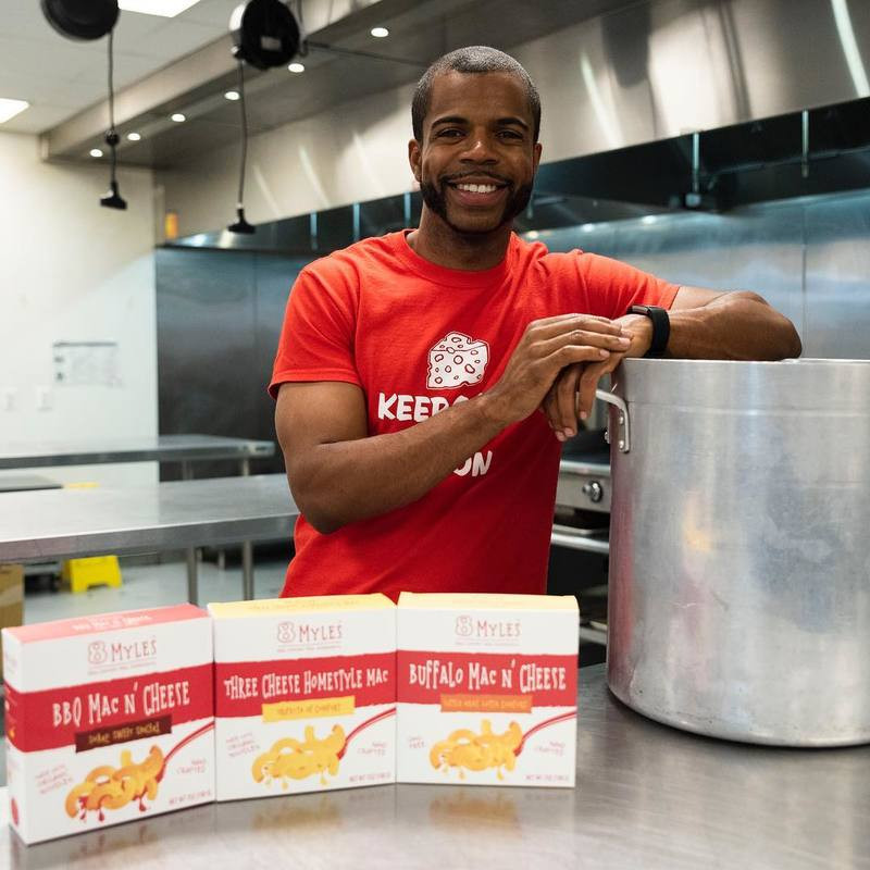 Myles Powell, owner of 8Myles poses with three of his mac and cheese flavors in an incubator kitchen