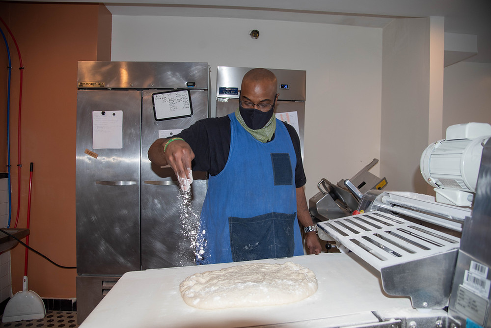 A baker sprinkles flour on dough at Rolling Pepperoni, a Pittsburgh bakery and Honeycomb alum