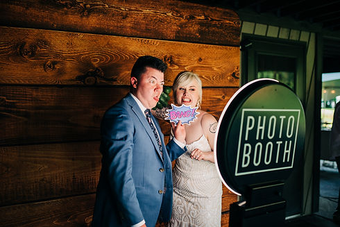 A bride and groom pose with props in front of GLOW photobooth