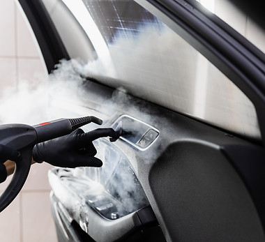 Steam vaping cleaning inside handle of car door after foam washing with brush. Worker in c