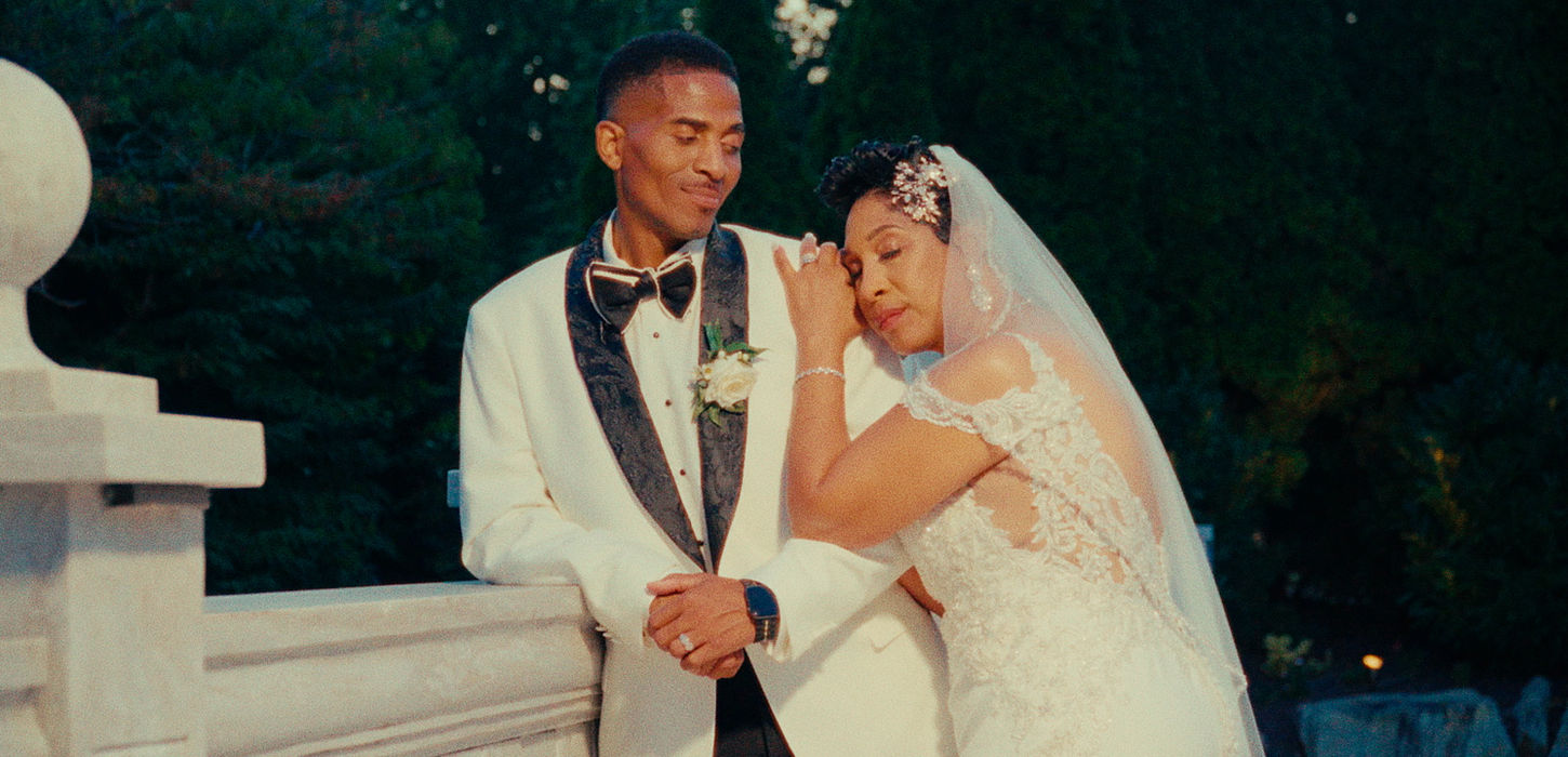 Patricia rests her hand on Charles’s shoulder beside a white railing.