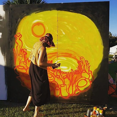 Rae spray painting a mural that looks like the start of a yin yang simbol with the sun in it