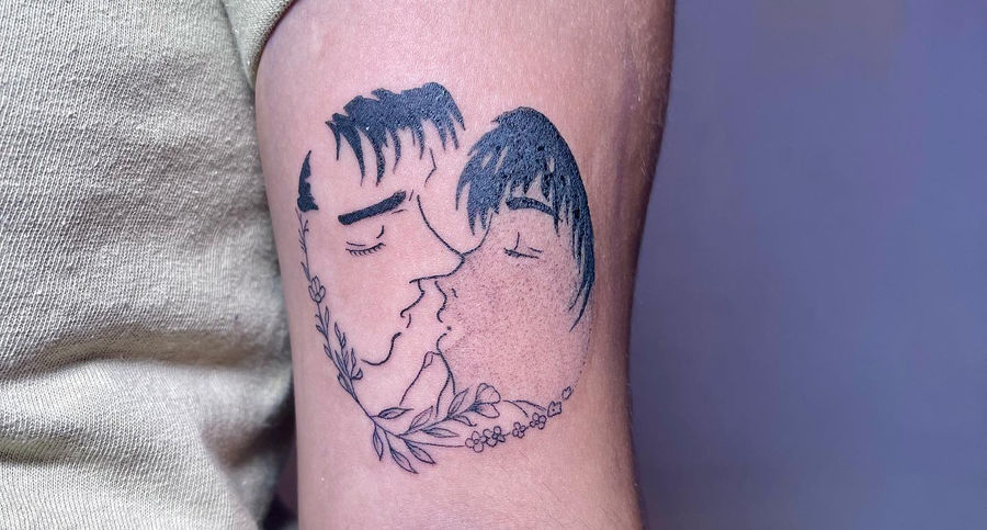 Two anime faces joined within leafy circle on upper arm tattoo