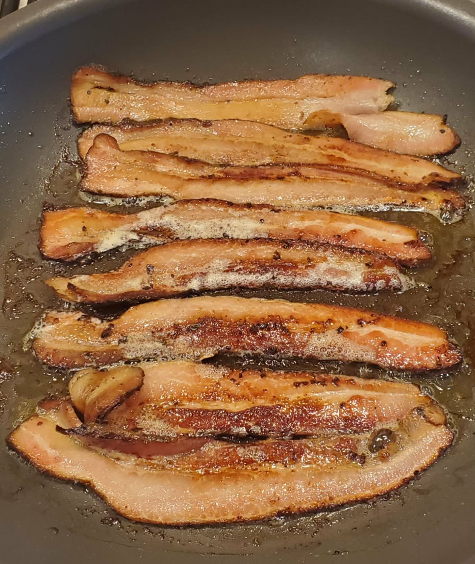 Home made bacon frying in a pan.