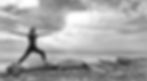 Black and white photo of yoga teacher standing on a beach with arms outstretched in Warrior 2 Pose