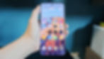 Hand holding a smartphone with colorful mountain wallpaper and various app icons. Blue background. Weather widget shows 29°C, cloudy.