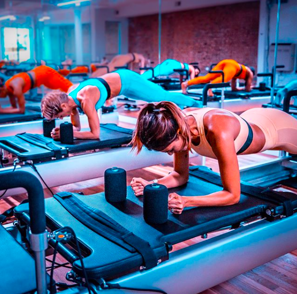 Group planks on reformers at BODYROK Midtown Colony Square Atlanta during upbeat class with teal lighting.