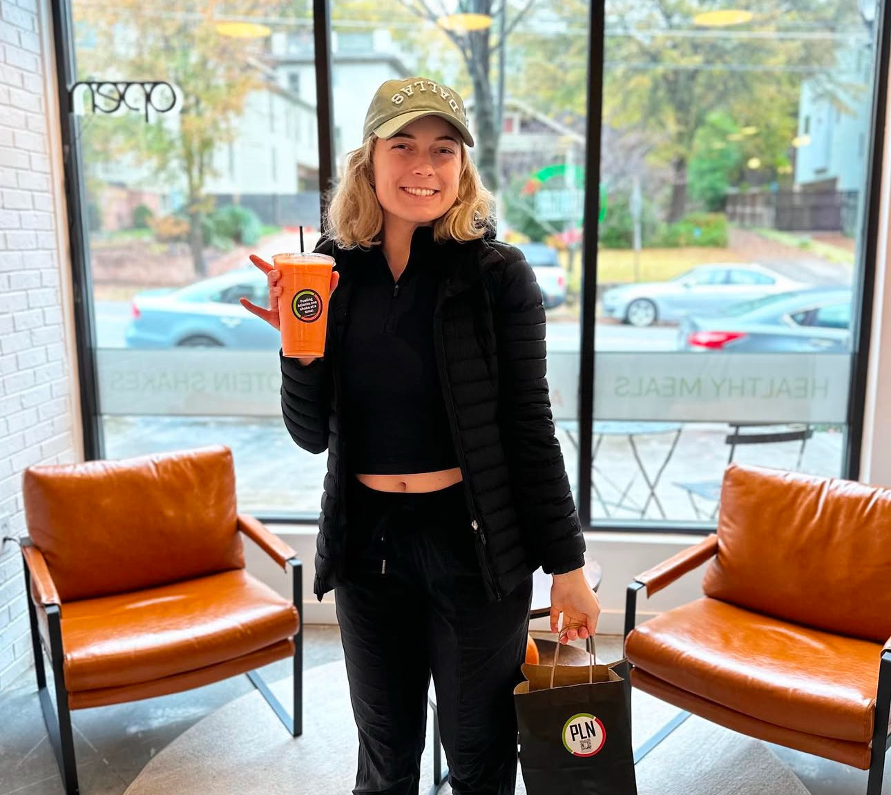 Woman drinking protein smoothie in bright lounge at Project LeanNation PLN Intown Atlanta.