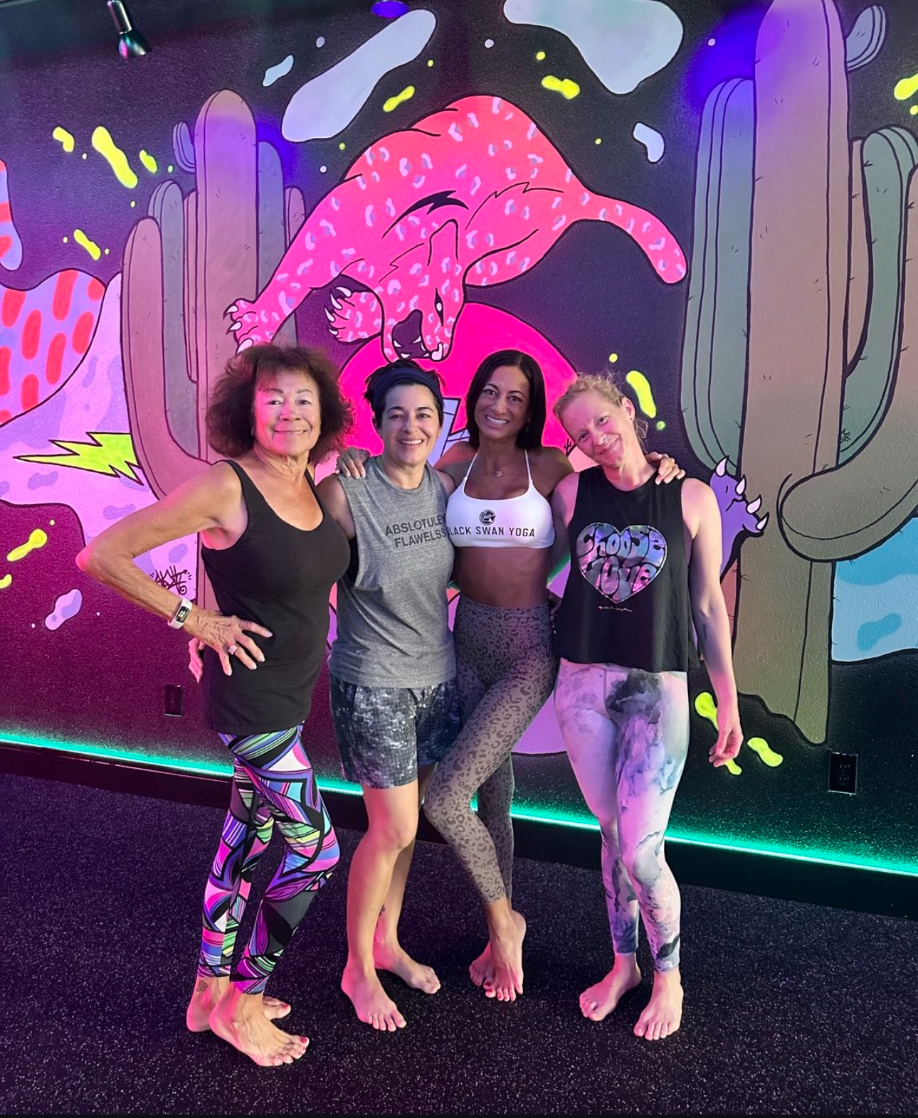Smiling yogis pose before bright dragon lotus mural at Black Swan Yoga Paradise Valley Phoenix.