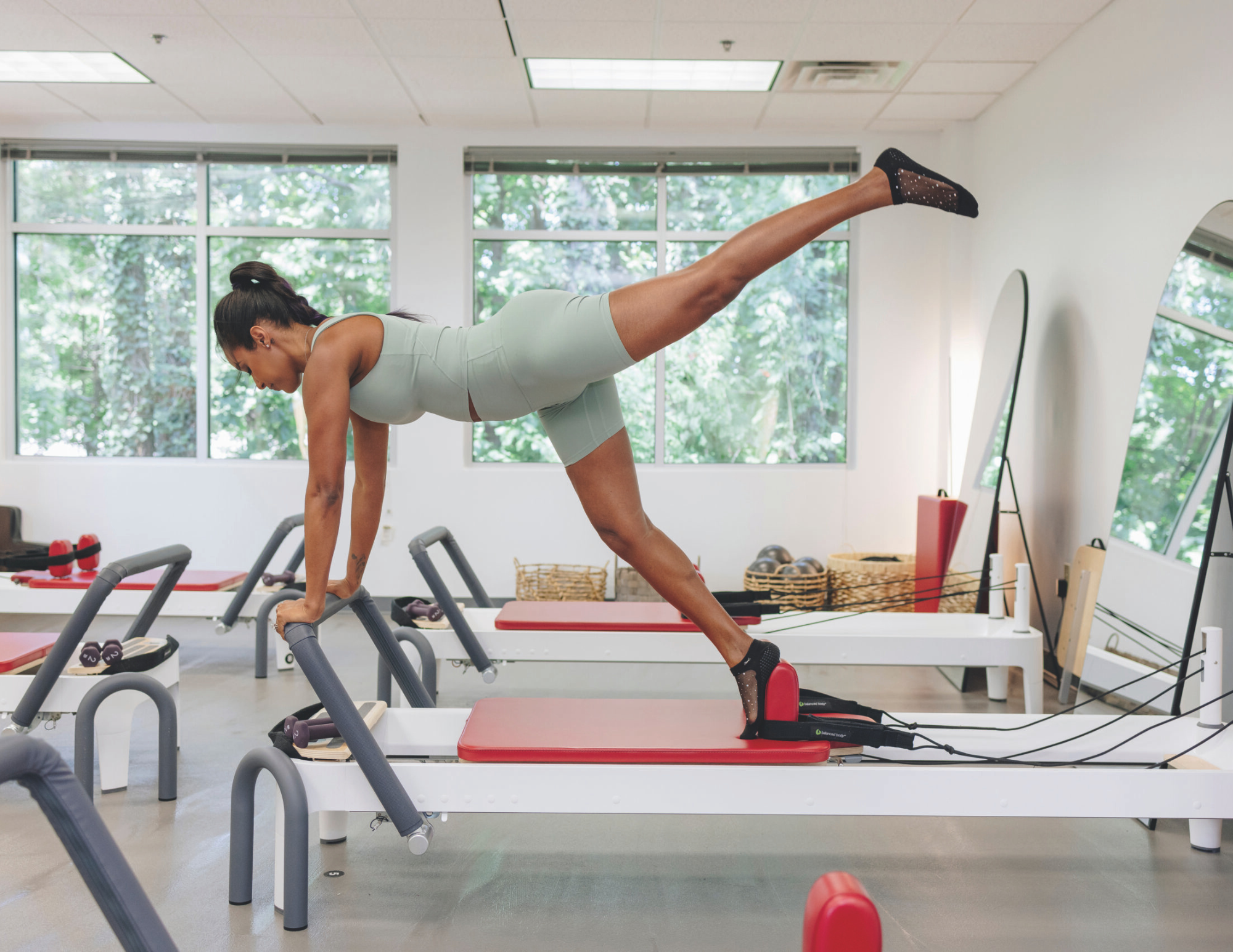 Instructor performs split jump on reformer demonstrating advanced move at Naked Mind Studio Roswell.