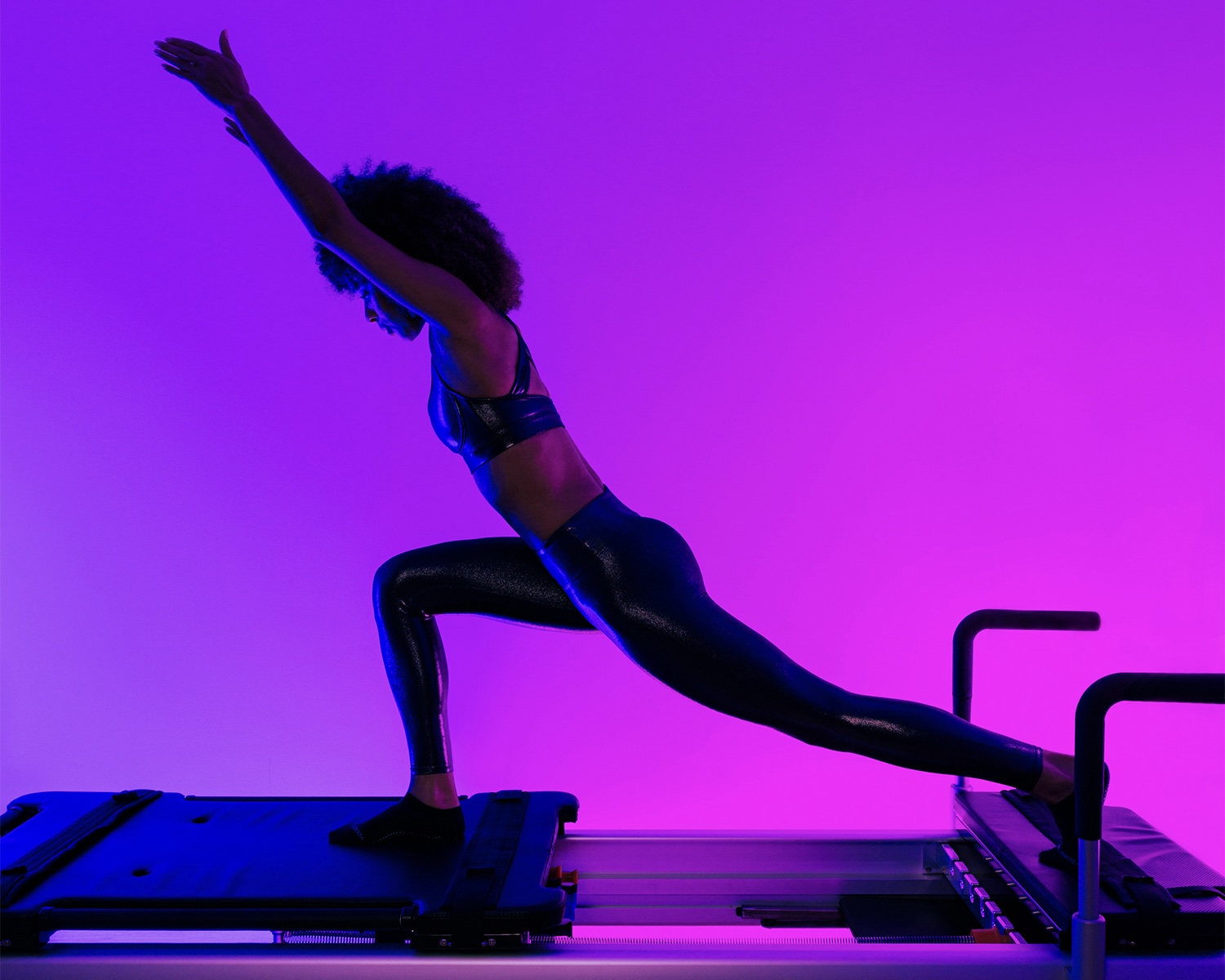 Athlete holds deep lunge on BODYROK reformer at Midtown Colony Square studio lit magenta.