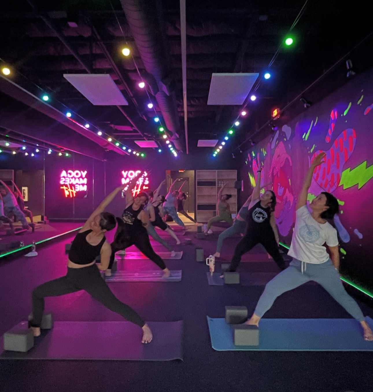Two yogis hold partner warrior pose on blocks during glow session at Black Swan Yoga Paradise Valley.