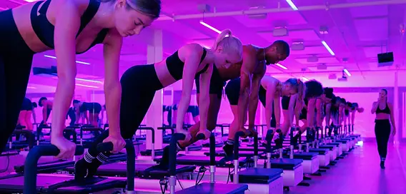 Clients bridging on BODYROK Midtown Colony Square reformers during evening class under purple lighting.