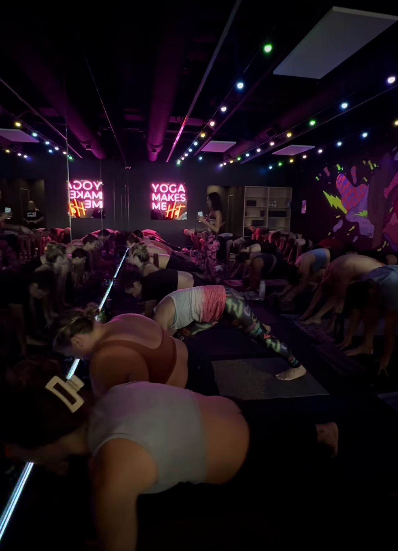 Packed glow class with pink lasers and yogis flowing on mats at Black Swan Yoga Paradise Valley Phoenix.