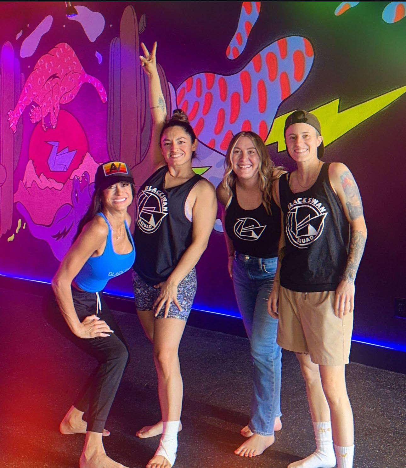Instructor team wearing studio tanks stands before neon mural at Black Swan Yoga Paradise Valley Phoenix.