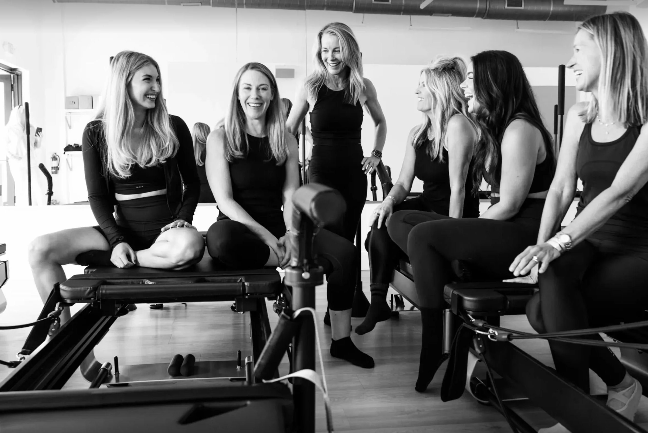 Team photo in black and white of women sitting on reformers at Evolve Modern Pilates Charleston.