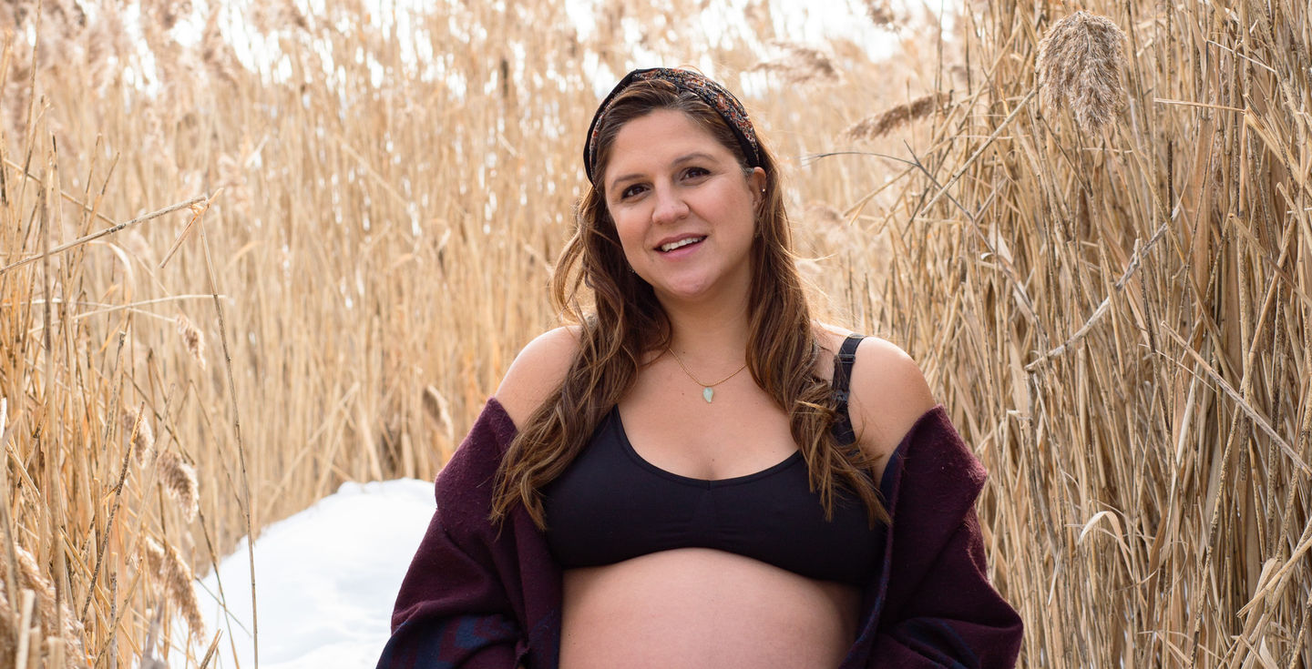 Pregnant woman sitting in a field of tall grass.