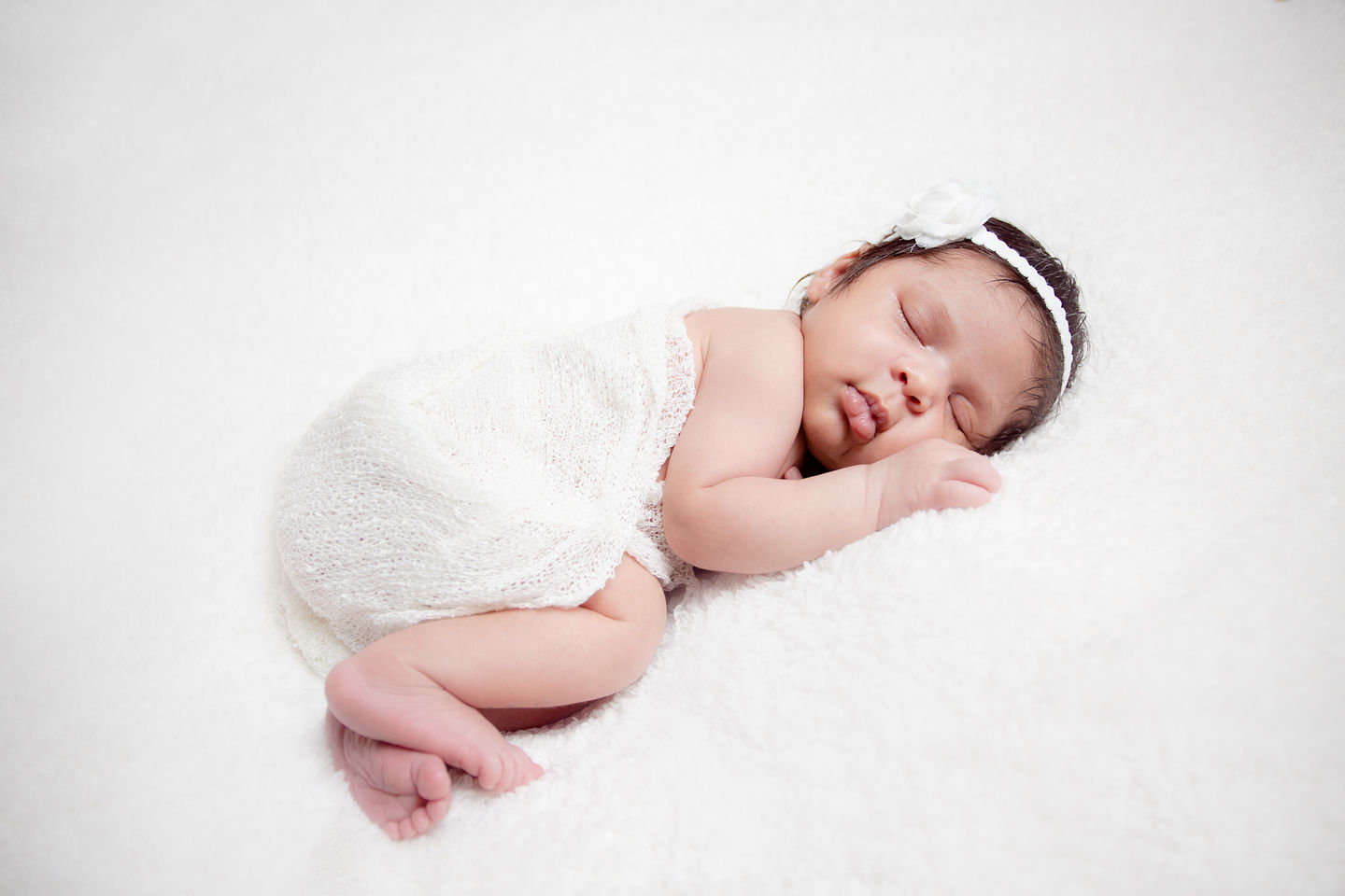 Sleeping baby wrapped in white, wearing a headband.