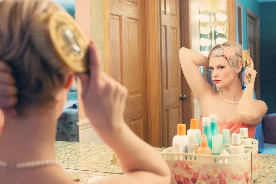 Woman combing hair home in front of a mirror