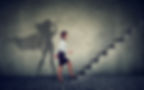 Super hero business woman stepping up on stairs climbing to success on gray wall backgroun