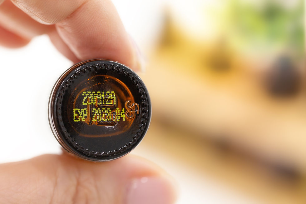 Close-up of fingers holding a brown bottle cap, showing yellow printed quality ID code text on the underside of dōTERRA essential oil bottle against a blurred background.