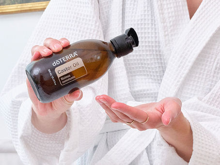 person wearing white bath robe pours castor oil into an open palm