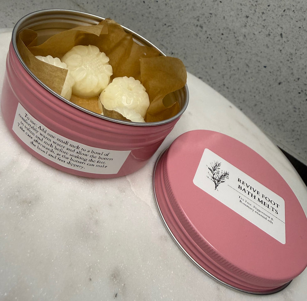 Open pink tin of white bath melts on a marble surface, with lid beside it labeled REVIVE FOOT BATH MELTS.