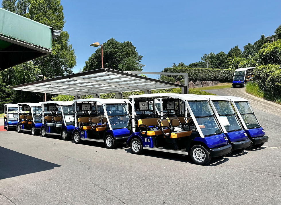 青空の下、屋根付き駐車場に青白いゴルフカートクーラー搭載車両がずらりと並び、奥の坂道にも1台走っている。番号117が見える。