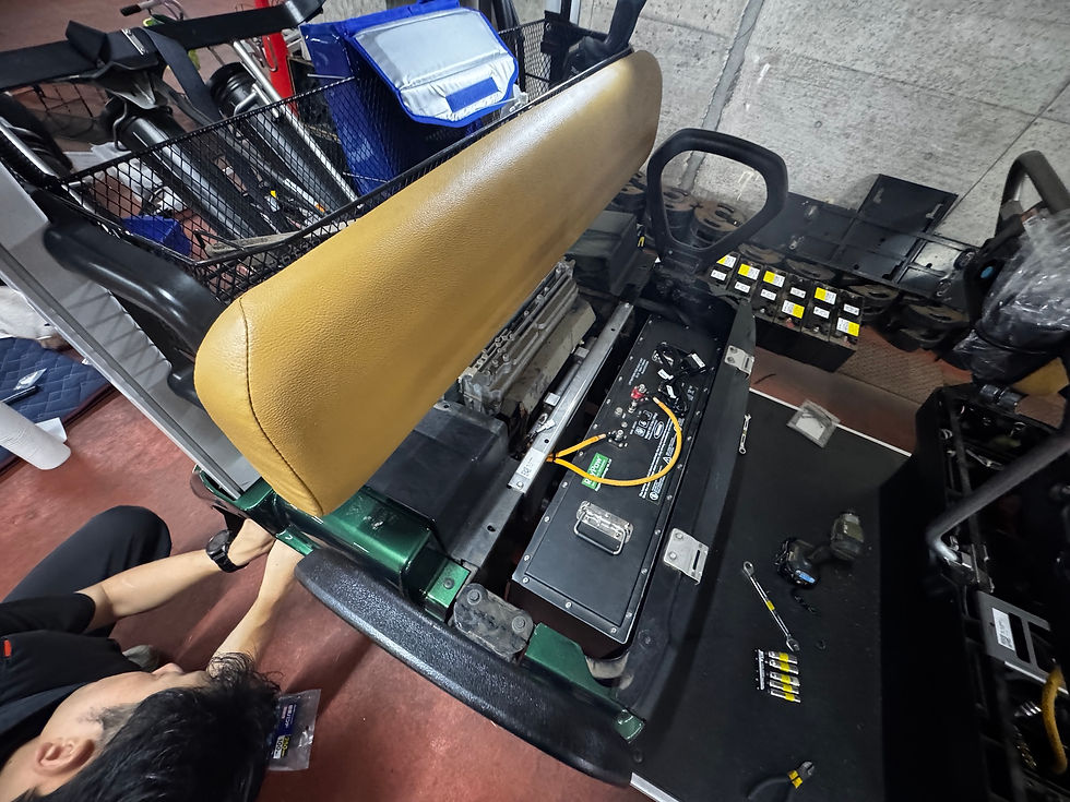 工場の床で、黄茶色のシートと電装部品を外した椅子台を整備する作業風景。工具や配線が周囲に散らばっている。