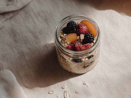 Szklany, szczelnie zamknięty słoik wypełniony kremową owsianką nocną z mlekiem roślinnym, borówkami i nasionami chia. Stoi na jasnym, lnianym obrusie w porannym świetle. Całość emanuje spokojem, troską i prostotą. Śniadanie, które czeka, aż znajdziesz chwilę dla siebie.