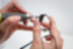 This header image shows a close up photograph of a glasses or optical glasses metal frame which has been broken. The frame is having a repair or fix by an eyewear repair specialist. The eyewear specialist is carefully extracting a frame screw.