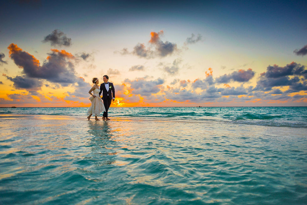 A newlywed couple walks on a beach at sunset