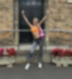 Amelia in gym clothes with a Pilates mat stood outside a church hall smiling