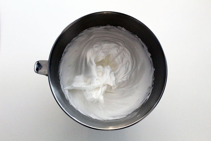 Assorted olive oil bottles on a wooden bench with a small bowl of golden oil and fresh olives.