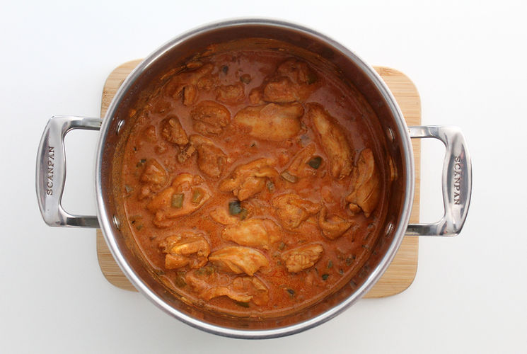 Adam Liaw’s Chicken Paprikash in a casserole dish, freshly cooked and steaming, resting on a wooden chopping board on a white kitchen bench top.