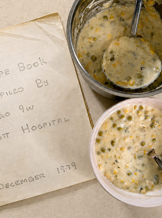 Overhead view of creamy Jiffy mussel chowder in a pale pink bowl, beside a saucepan and handwritten Hutt Hospital recipe book dated December 1979.