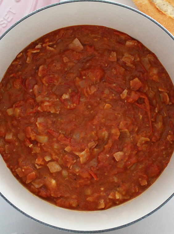 Tomato and bacon stew with diced onion in a pink Le Creuset casserole dish