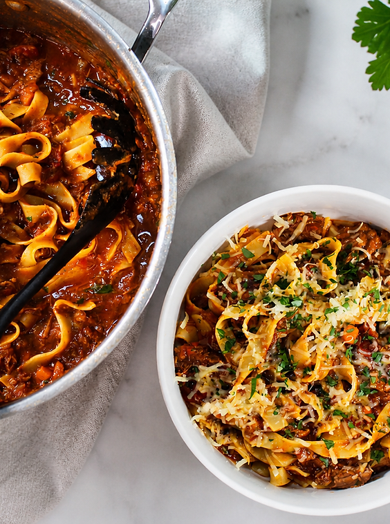 Slow-cooked beef ragu with tagliatelle, grated Parmesan and herbs beside the cooking pot