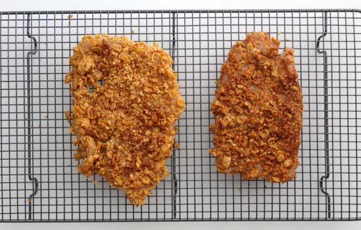 Two chicken cutlets coated in cornflake crumbs resting on a wire rack, ready to cook — Simply Nigella recipe test.