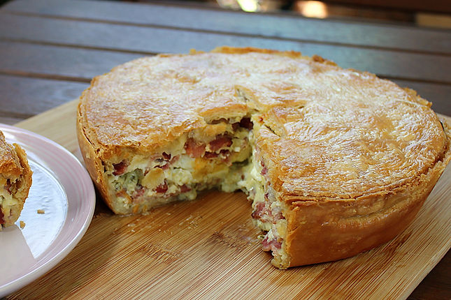 Golden bacon and egg pie with a slice removed, showing the bacon, egg and creamy cheese sauce filling.