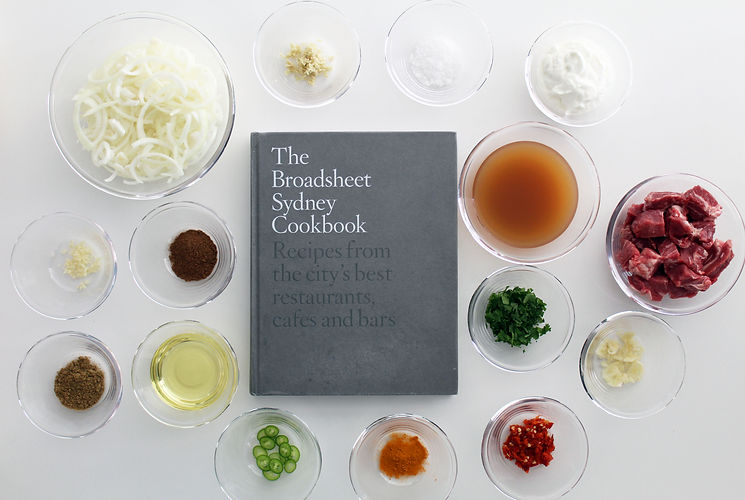A copy of The Broadsheet Sydney Cookbook on a white benchtop surrounded by fresh ingredients for one of the recipes.